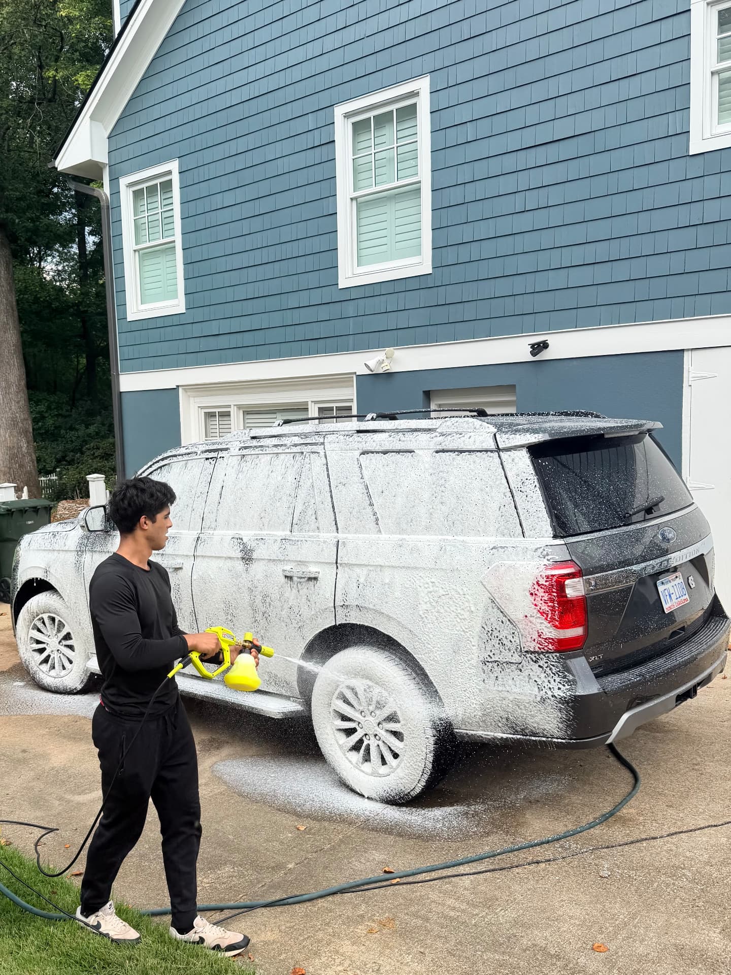 A Good Fellas detailer foaming up a dark SUV in a Raleigh driveway